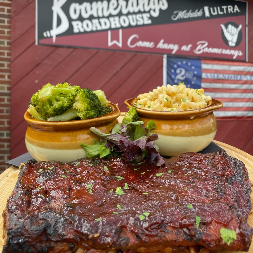 Glazed barbecue ribs with broccoli and creamy macaroni in ceramic bowls, displayed beneath a Bonnerdaddy’s Roadhouse sign.